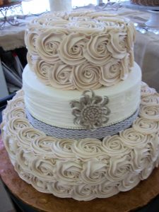 ivory wedding cake with white tier in between two ivory creme roses tiers